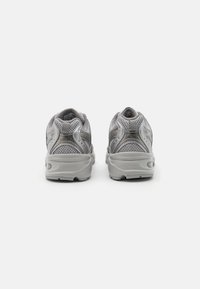 Zapatillas deportivas grises con una parte superior de malla para transpirabilidad, suela acolchada y acentos reflectantes en el talón y los laterales.