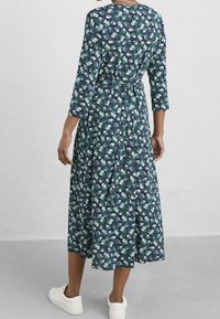 Laivastonsininen kukkakuvioinen maksimekko, jossa on kolme neljäsosaa hihat, vyötäröllä kiristettävä nauha ja laskeutuva helma. Yhdistetty valkoisiin tennareihin.