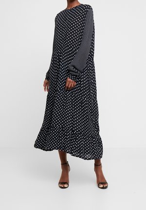 Schwarzes Kleid mit langen Ärmeln und Polka-Punkten, mit ausgestelltem Saum, aus leichtem Stoff gefertigt und mit unterschiedlichen Polka-Punkt-Mustern verziert.