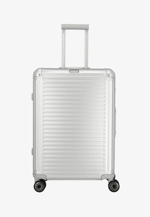 Zilveren harde koffer met verticale groeven, uitschuifbaar handvat en vier draaiwielen voor gemakkelijke mobiliteit.