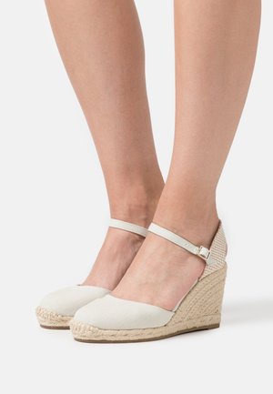 Bílé plátěné espadrilové wedges s kulatou špičkou, vypletenou jutu jako středovou část a úzkým kotníkovým páskem. Texturovaný akcent na patě dodává detail.