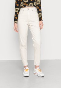 Ljust beige jeans med hög midja och avsmalnande ben, tillverkade av bomullsdenim. Kombinerat med en svart blommig crop top och vita sneakers.