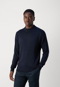 Navy blue knit sweater with a crew neck, long sleeves, and ribbed cuffs. Features a textured fabric and a subtle logo detail on the sleeve.