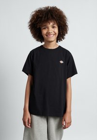 Svart bomulls t-shirt med korta ärmar, rund hals och liten logga p�å bröstet, tillsammans med ljusgrå shorts. Slät textur.