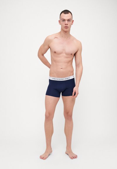 Námořnické modré boxerky s bílým pasem s logem "POLO RALPH LAUREN". Hladká tkanina s přiléhavým střihem. Model pózuje ve stoje.