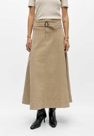 Falda beige de talle alto con cinturón y botines negros de tacón, llevada por una persona con una camiseta beige de manga corta.