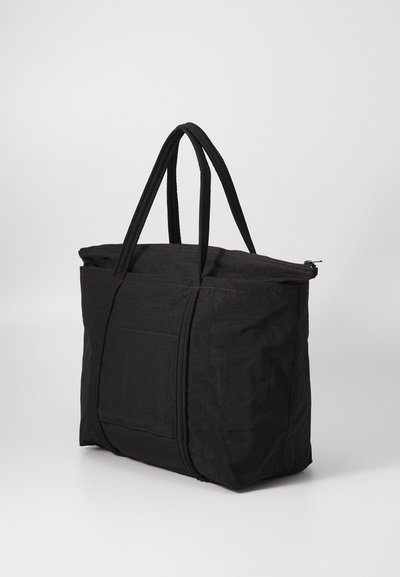 Black tote bag featuring a rectangular shape, textured fabric, zip closure, and double handles. Includes a front pocket with stitching detail.