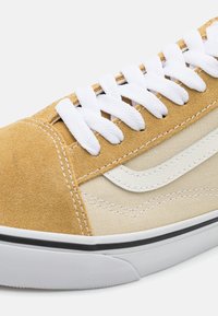 Sneaker mit einem hellbraunen Wildleder-Obermaterial und beigefarbenen Canvas-Seiten, ausgestattet mit weißen Schnürsenkeln, kontrastierenden Nähten und einer schwarzen Gummisohle.