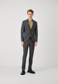 Gray suit with a tailored fit and notch lapels, paired with a tan shirt. Model wearing black dress shoes, set against a plain background.
