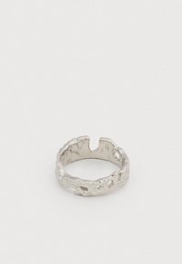 Ασημένιο δαχτυλίδι με ανοιχτή μπάντα και υφή, με ακανόνιστο, οργανικό σχέδιο κοπής, τοποθετημένο σε λευκή επιφάνεια.