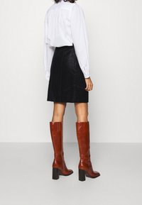 Marron nahka polvipituiset saappaat, joissa on paksu korko, sileä pinta ja pystysuunnassa uurrettu yksityiskohta ylhäällä, yhdistetty mustaan mokkanaisarkkiin.