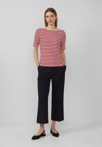 Haut à manches courtes rayé rouge et blanc, coupe décontractée, associé à un pantalon large noir. Le modèle se tient les mains dans les poches.