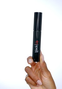 Tube de mascara noir tenu dans une main, forme cylindrique, finition noire brillante, fond blanc, étiquette avec "black Up" en lettres rouges.