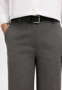 Szare eleganckie spodnie o gładkiej fakturze, z bocznymi kieszeniami oraz czarnym skórzanym paskiem z metalową klamrą. Widoczna biała koszula na guziki.