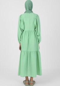 Vihreä kerroksellinen mekko, jossa on pitkät puff-hihat, kerätty vyötärö ja napitus takana. Yhdistettynä matching vihreän huivin ja sandaalien kanssa.