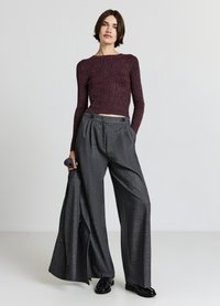 Bordeauxrotes, geripptes Crop-Top mit langen Ärmeln, kombiniert mit lockeren, hoch taillierten grauen Hosen; die Hose weist ein dezentes Muster und eine Doppelknopf-Details auf.
