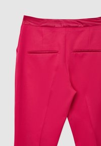 Pantalons roses vifs avec une texture lisse, présentant deux poches arrière cachées et une taille en satin pour plus de détail.