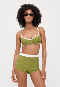 Grønn ripset bikini sett med en bh med hvit kant og justerbare stropper, kombinert med høytalere shortser med hvit livlinje.