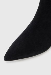 Svart semsket spiss tå sko med en glatt tekstur og elegant design, som har en stiletthæl og et minimalistisk silhuett.