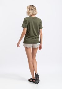 T-shirt in cotone verde oliva con maniche corte, vestibilità morbida e scollatura rotonda, abbinata a pantaloncini beige chiaro e sandali neri.