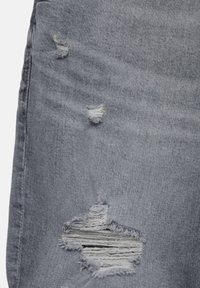 Tissu en denim gris clair avec trois zones usées, dont une grande déchirure horizontale laissant apparaître des fils blancs.