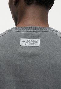 Γκρι φούτερ με ριμπ λαιμόκοψη, που διαθέτει λευκή ετικέτα με το λογότυπο και τη φράση "Adidas Originals" στο πίσω μέρος, ύφασμα με ομαλή υφή.