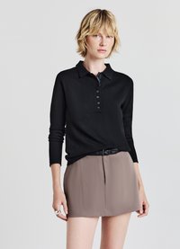 Polo a maniche lunghe nera con colletto e patta con cinque bottoni, abbinato a una gonna beige a vita alta e una cintura nera.