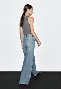 Grå ärmlös topp ihop med ljusblå, högmidjade jeans med vida ben. Slät denimtextur, klassisk design med fem fickor och sömmar.