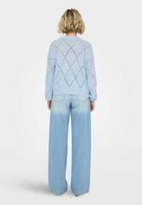 Pull tricoté bleu clair avec motif en losange ; associé à un jean large bleu clair présentant un dégradé de foncé à clair.