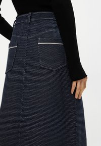 Τζιν φούστα σε ναυτικό μπλε με υφή. Διαθέτει δύο πίσω τσέπες με λευκές ραφές και στενό μέσο.