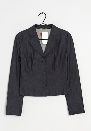 Ciemnoszara damska marynarka z trzema guzikami, kołnierzem z wycięciem, długimi rękawami, wisząca na czarnym wieszaku z białą metką na białym tle.