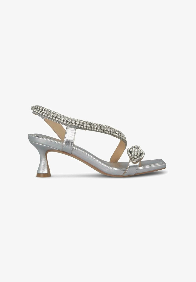 Sandal metallic en plata con tirante adornado con piedras de strass, tacón bajo y puntera cuadrada con un acento en forma de corazón.