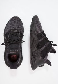 Black athletic shoes with a textured knit upper, suede accents, and a geometric rubber sole. Features laces and logo on the tongue.