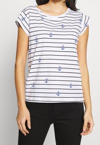 Vit bomull t-shirt med horisontella svarta ränder och blå ankartryck. Kappärmar och avslappnad passform. Enkel rund halsringning.