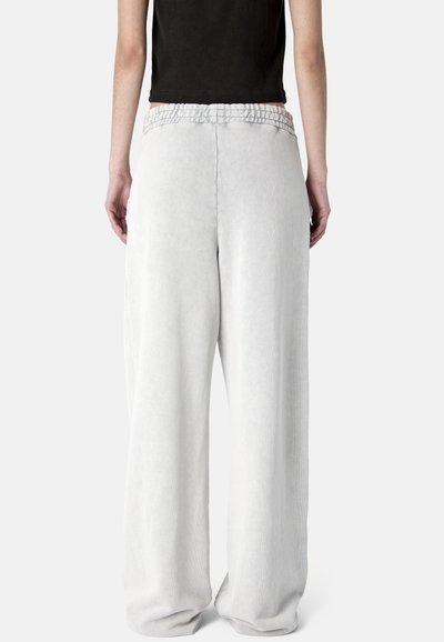 Personne portant un pantalon large et ample gris clair avec une taille élastique, vue de dos sur un fond blanc uni.