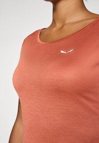 Kortärmad t-shirt med rund hals i ett mjukt, persikofärgat tyg med subtil struktur och en vit logotypaccent på bröstet.