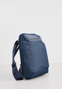 Piccola borsa a tracolla blu navy con tessuto testurizzato, chiusura con zip, tracolla regolabile e un accent logo sul davanti.