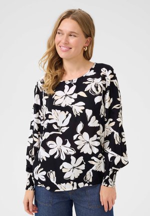 Blouse noire avec motif floral blanc, encolure ronde, manches longues avec poignets élastiques et coupe décontractée. Texture lisse, tissu léger.