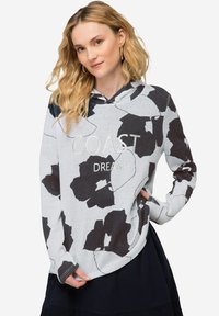 Witte hoodie met een zwart bloemenpatroon en de tekst "COAST DREAM" op de borst. Zachte textuur, ontspannen pasvorm.