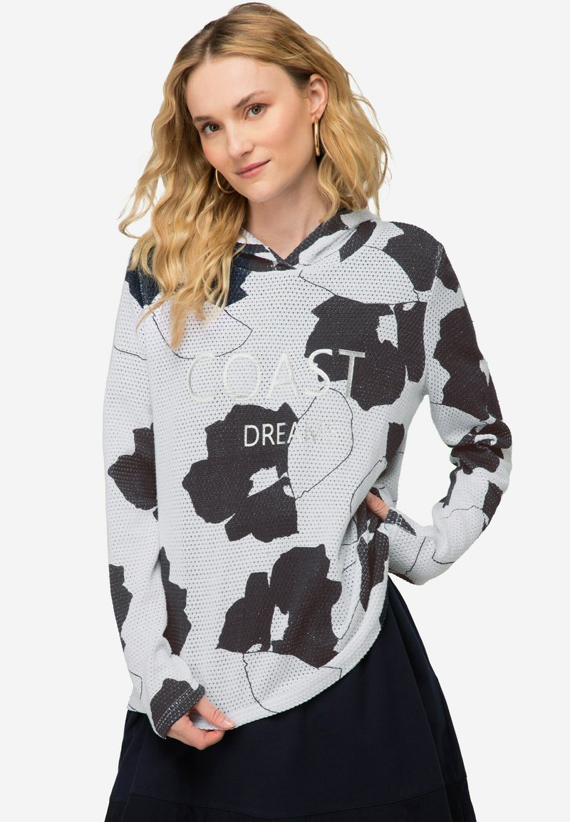 Witte hoodie met een zwart bloemenpatroon en de tekst "COAST DREAM" op de borst. Zachte textuur, ontspannen pasvorm.