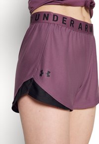 Pantalones cortos deportivos morados con una cintura de marca negra, que presentan un diseño en capas con forro interior negro y una textura ligeramente brillante.