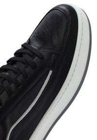 Czarne skórzane sneakersy o gładkim wykończeniu, z płaskimi czarnymi sznurówkami, białym detalem wzdłuż boku oraz białą gumową podeszwą.