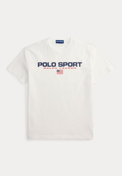 Λευκό βαμβακερό μπλουζάκι με τη φράση "POLO SPORT" σε ναυτικό μπλε και "RALPH LAUREN" σε κόκκινο. Περιλαμβάνει ένα μικρό γραφικό με την αμερικανική σημαία. Κοντά μανίκια, στρογγυλή λαιμόκοψη.