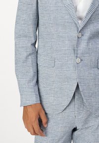 Light blue plaid suit made of textured fabric, featuring two buttons, a notch lapel, and a single pocket on the left side of the jacket.