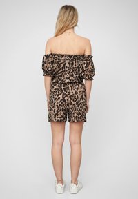 Jumpsuit à imprimé léopard, décolleté asymétrique, avec des manches bouffantes, une taille élastique, et des shorts. Tissu léger dans des tons de marron et noir.