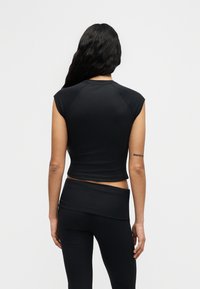 Μαύρο ριμπ τοπ crop με κοντά μανίκια, συνδυασμένο με μαύρο κολάν ψηλόμεσο. Λείο υλικό, εφαρμοστό σχέδιο και ελάχιστες λεπτομέρειες.