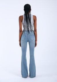 High-waisted light blue flared jeans with a smooth denim texture, featuring back pockets and a snug fit around the waist and hips.