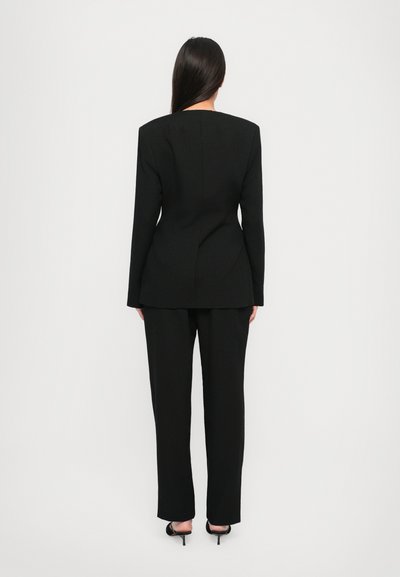Zwarte op maat gemaakte suit met scherpe schouders, lange mouwen en een rechte broek, vervaardigd uit een gladde stof, van achteren weergegeven.