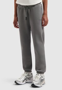 Grijze sweatpants van zachte stof met een elastische tailleband, zijzakken en elastische boorden bij de enkels; gecombineerd met zilveren sneakers.