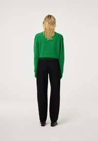 Groene fuzzy gebreide trui met lange mouwen, gecombineerd met zwarte, losse broeken. Eenvoudig ontwerp, zonder zichtbare logo's of patronen.